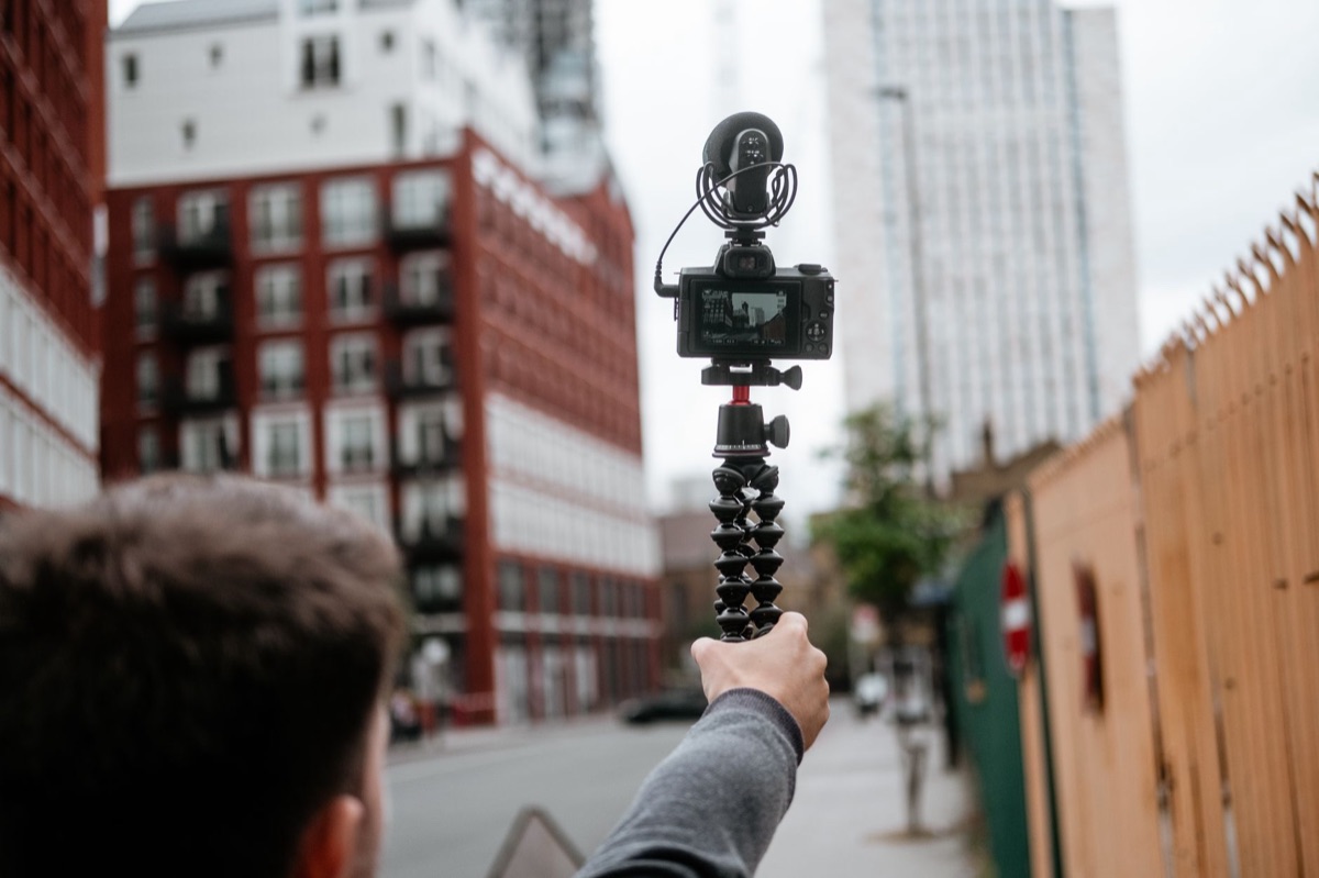 A person holding a compact action camera on a handheld gimbal stabilizer during a hike.