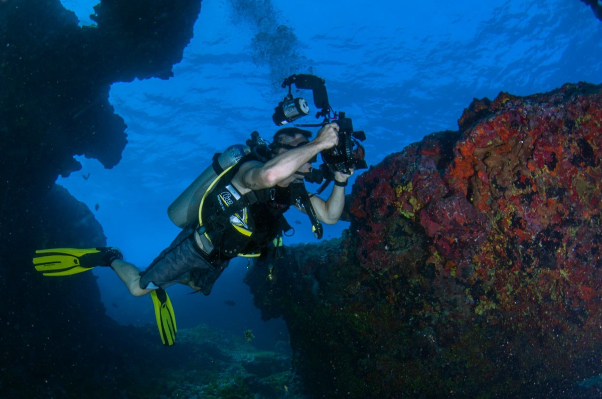 Cámara de acción sumergida bajo el agua con burbujas y arrecife de coral al fondo.