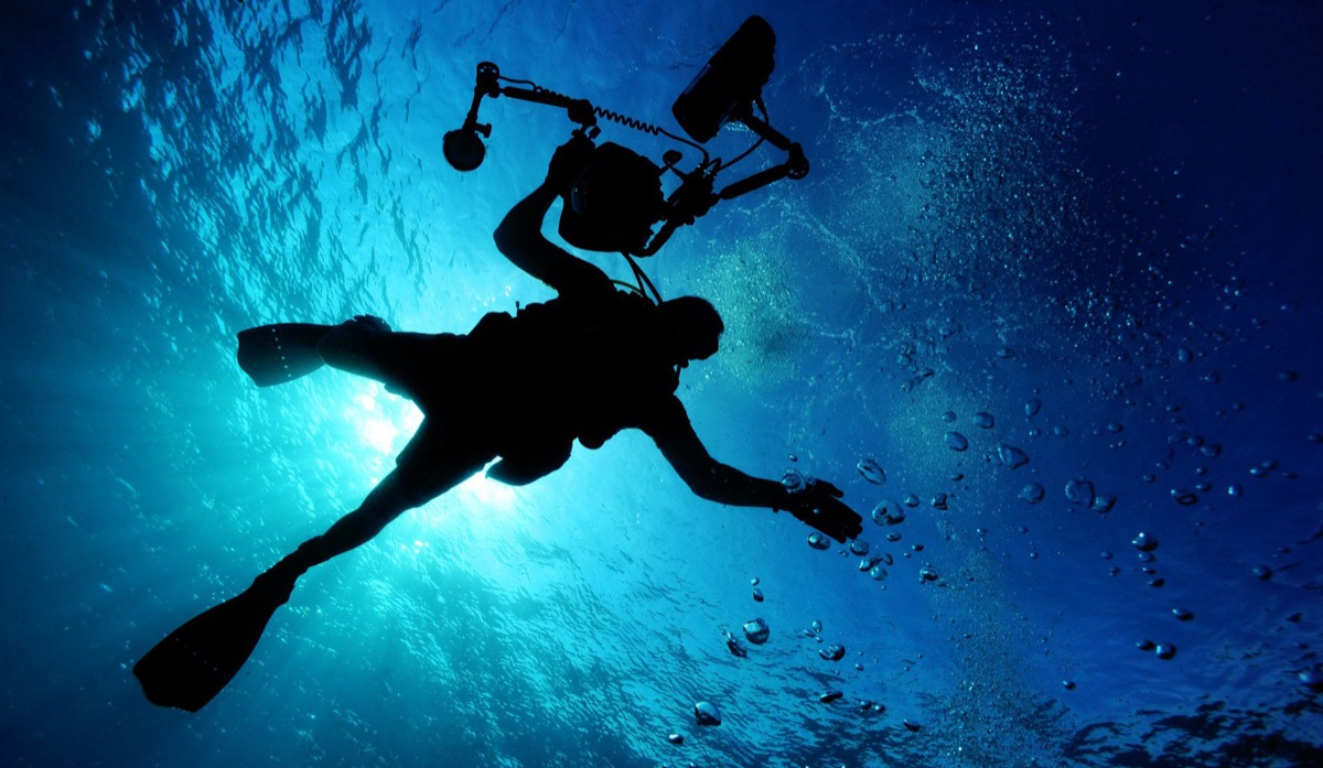 An action camera submerged in clear blue ocean water near coral reefs.