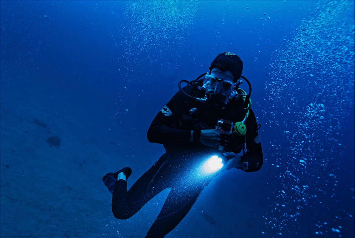 Câmera de ação submersa em água cristalina com corais ao fundo.