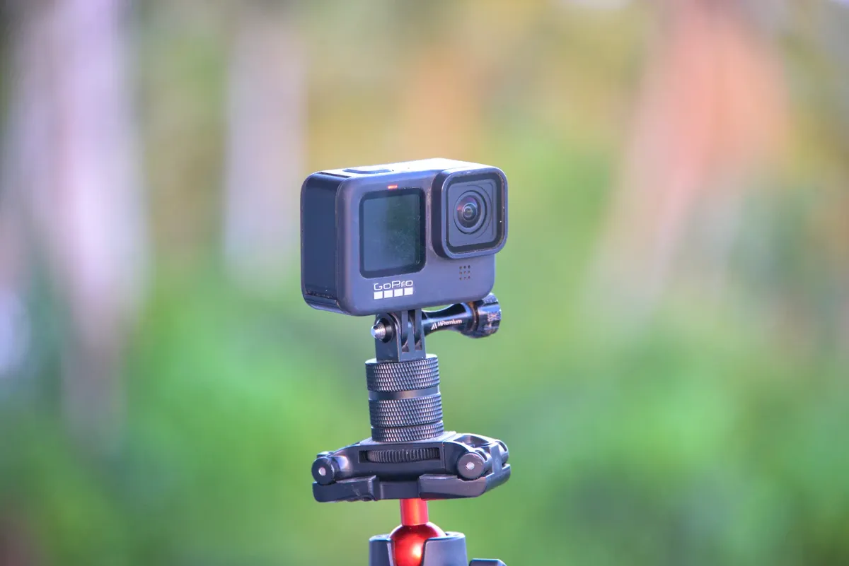 Close-up of a GoPro action camera mounted on a tripod set against a blurred outdoor background.